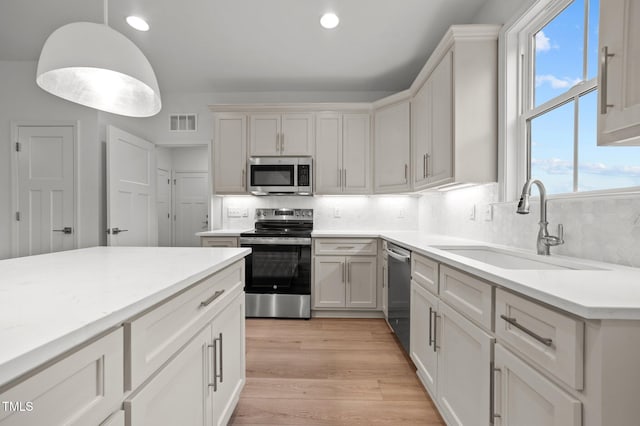 kitchen featuring sink, light hardwood / wood-style flooring, appliances with stainless steel finishes, tasteful backsplash, and white cabinets