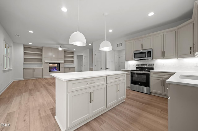 kitchen featuring a multi sided fireplace, appliances with stainless steel finishes, pendant lighting, ceiling fan, and light hardwood / wood-style flooring