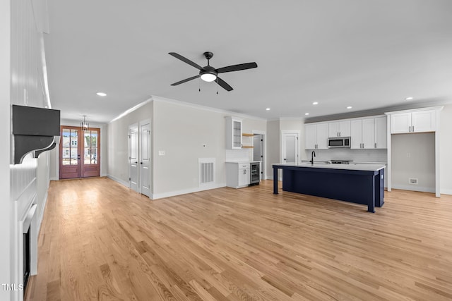 unfurnished living room with a sink, visible vents, baseboards, light wood-style floors, and ornamental molding