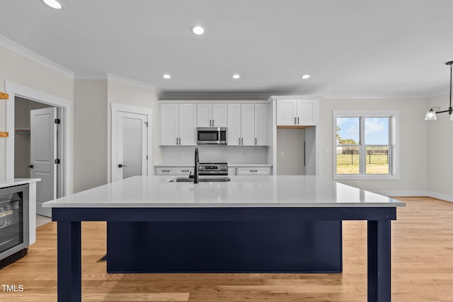 kitchen featuring white cabinets, wine cooler, stainless steel microwave, crown molding, and a sink