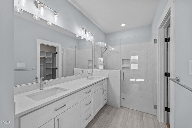 bathroom featuring double vanity, a stall shower, a sink, and a walk in closet