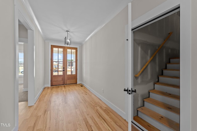 entryway with french doors, light wood-style floors, ornamental molding, baseboards, and stairs