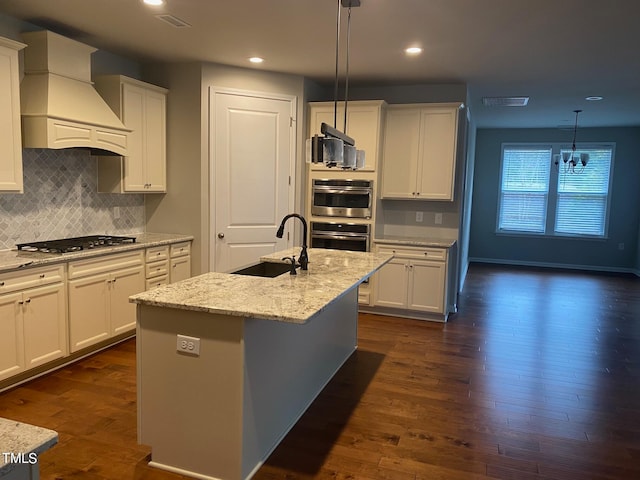 kitchen featuring a center island with sink, appliances with stainless steel finishes, premium range hood, and white cabinetry