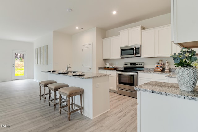 kitchen with appliances with stainless steel finishes, white cabinets, a kitchen island with sink, and light stone countertops