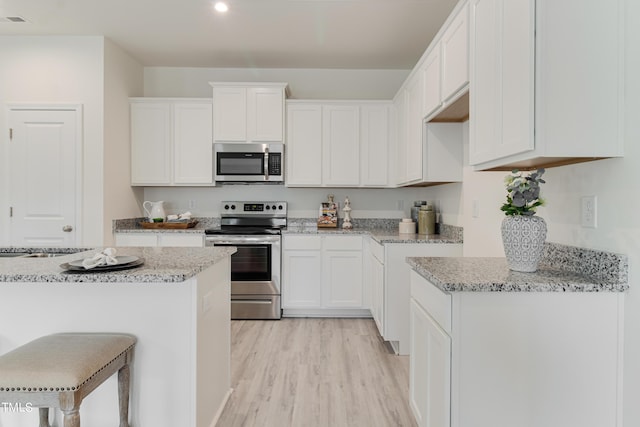 kitchen with light stone counters, stainless steel appliances, white cabinetry, a kitchen breakfast bar, and light wood finished floors