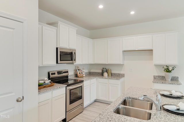 kitchen with white cabinets, light stone counters, stainless steel appliances, a sink, and recessed lighting