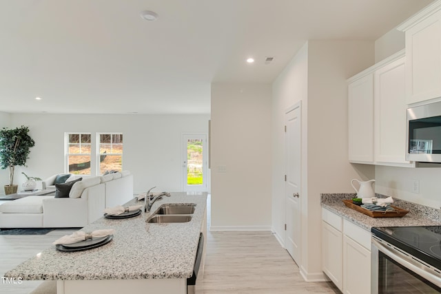 kitchen with open floor plan, white cabinets, a sink, and an island with sink