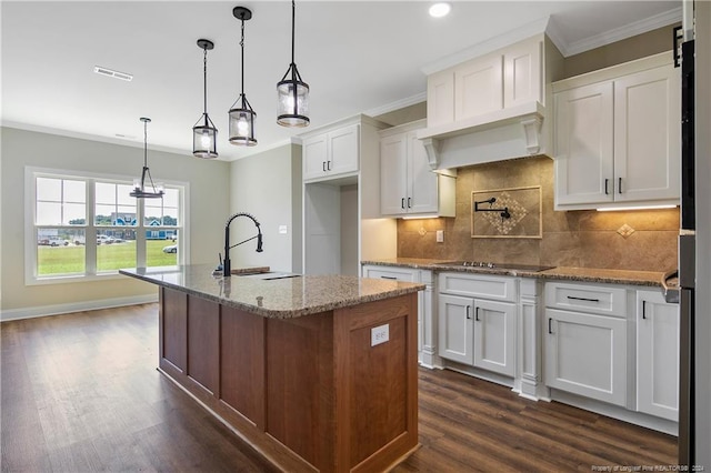 kitchen featuring light stone countertops, pendant lighting, an island with sink, and white cabinetry