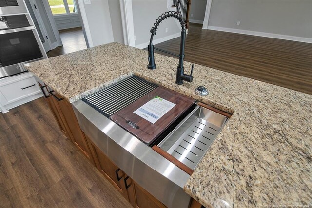 details featuring light stone counters, dark hardwood / wood-style flooring, oven, and sink