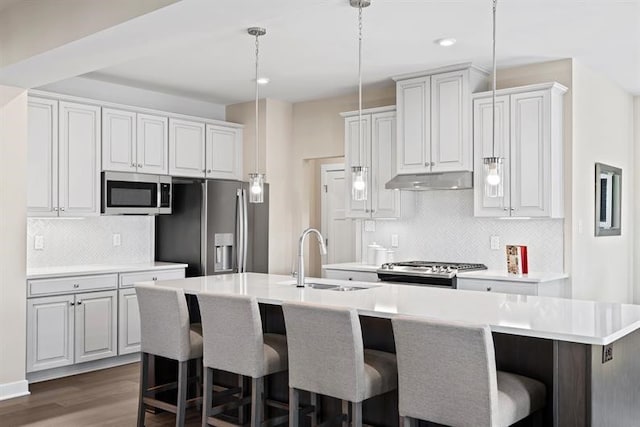 kitchen featuring sink, stainless steel appliances, decorative light fixtures, a breakfast bar area, and a kitchen island with sink