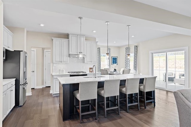 kitchen with a center island with sink, white cabinets, sink, hanging light fixtures, and stainless steel refrigerator