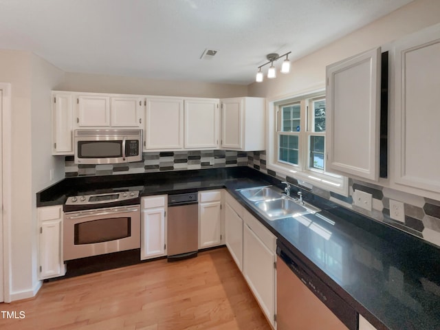 kitchen with appliances with stainless steel finishes, tasteful backsplash, sink, light wood-type flooring, and white cabinets