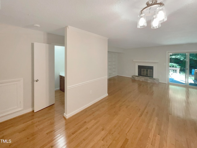 unfurnished living room featuring light wood-type flooring, a textured ceiling, and an inviting chandelier