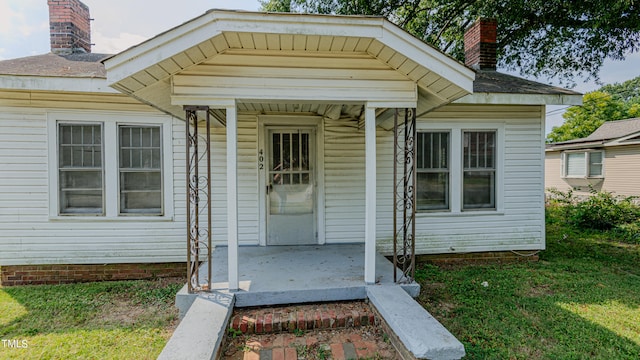 view of exterior entry with a porch and a lawn