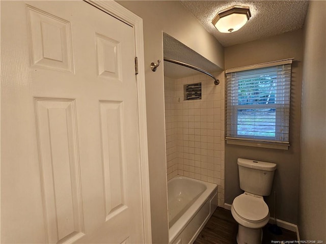 bathroom with a textured ceiling, toilet, and tiled shower / bath