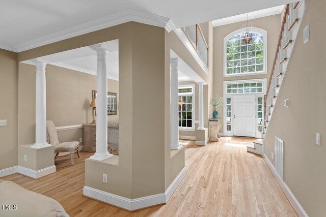 foyer entrance featuring light wood-type flooring, crown molding, a chandelier, and decorative columns