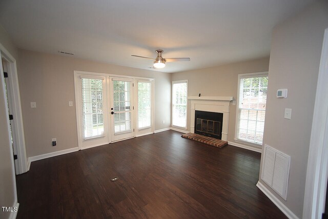 unfurnished living room featuring ceiling fan, plenty of natural light, a fireplace, and dark hardwood / wood-style flooring