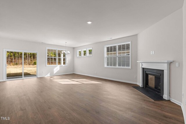 unfurnished living room with a wealth of natural light, an inviting chandelier, and dark hardwood / wood-style floors