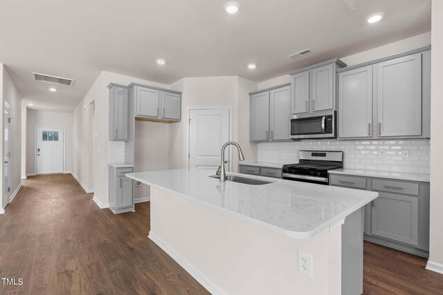 kitchen with stainless steel appliances, light stone counters, sink, dark hardwood / wood-style floors, and a center island with sink