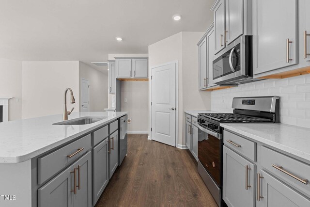 kitchen featuring dark hardwood / wood-style floors, a kitchen island with sink, stainless steel appliances, sink, and light stone counters