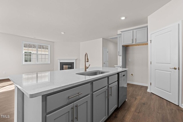 kitchen featuring dishwasher, light stone countertops, sink, dark hardwood / wood-style floors, and an island with sink