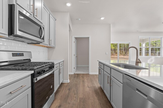 kitchen with backsplash, appliances with stainless steel finishes, sink, gray cabinets, and dark hardwood / wood-style floors