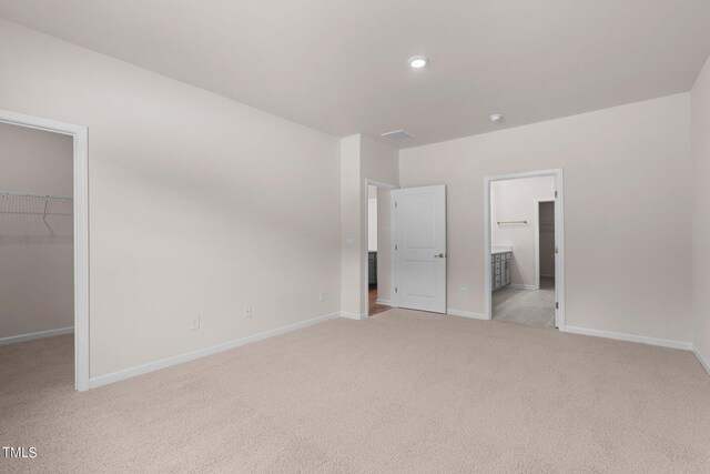 unfurnished bedroom with a walk in closet, light colored carpet, ensuite bathroom, and a closet