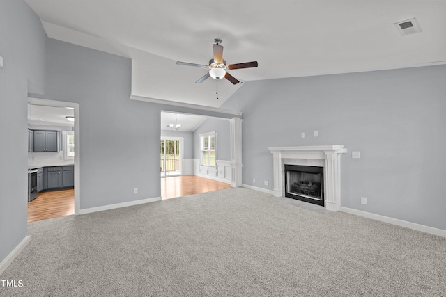 unfurnished living room with ceiling fan with notable chandelier, a premium fireplace, light carpet, and vaulted ceiling