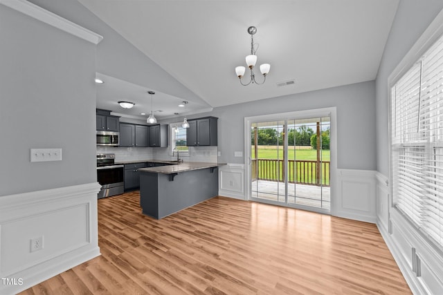 kitchen featuring decorative light fixtures, stainless steel appliances, kitchen peninsula, lofted ceiling, and a breakfast bar area