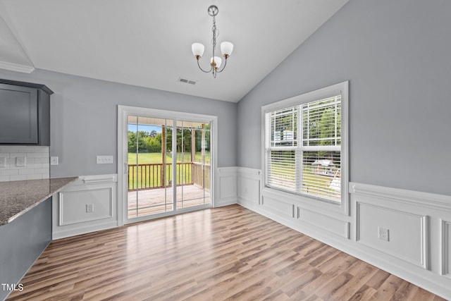 unfurnished dining area with lofted ceiling, hardwood / wood-style flooring, and a notable chandelier