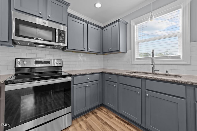 kitchen with dark stone counters, crown molding, stainless steel appliances, sink, and light hardwood / wood-style floors