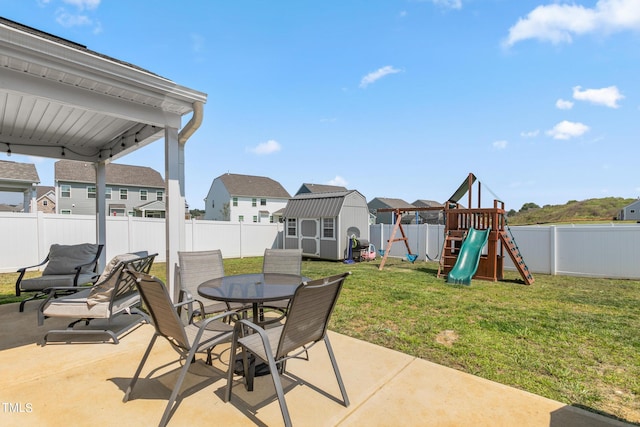 view of patio / terrace featuring an outbuilding, a playground, a fenced backyard, a shed, and outdoor dining space