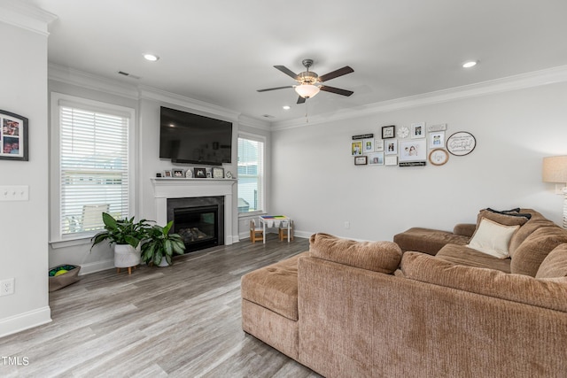 living room featuring visible vents, baseboards, a glass covered fireplace, ornamental molding, and light wood-style floors