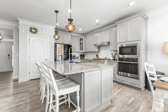 kitchen with decorative backsplash, stainless steel appliances, gray cabinetry, under cabinet range hood, and a sink