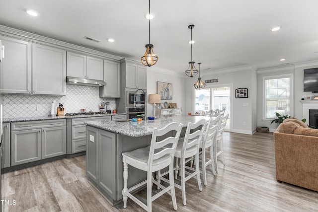 kitchen featuring light wood-style flooring, ornamental molding, gray cabinets, under cabinet range hood, and backsplash