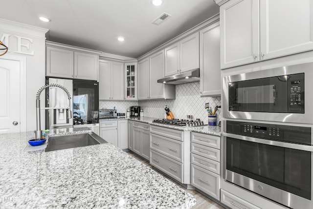 kitchen featuring stainless steel appliances, gray cabinets, visible vents, a sink, and under cabinet range hood