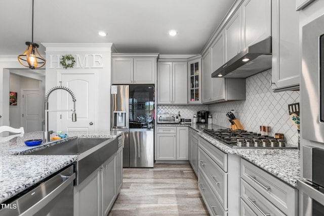 kitchen featuring stainless steel appliances, gray cabinets, backsplash, a sink, and wall chimney exhaust hood