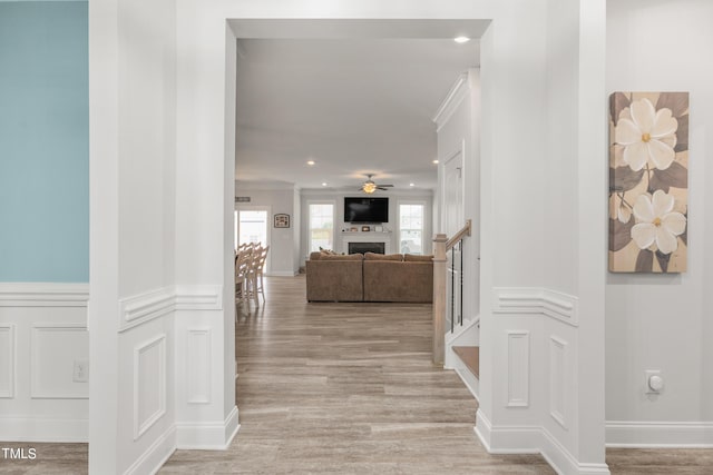 corridor featuring a wainscoted wall, stairway, light wood-type flooring, a decorative wall, and recessed lighting