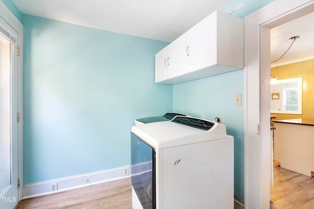 laundry area featuring light wood-type flooring, washing machine and clothes dryer, and cabinets