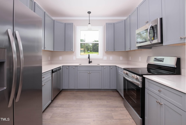 kitchen with gray cabinetry, light hardwood / wood-style floors, hanging light fixtures, stainless steel appliances, and sink