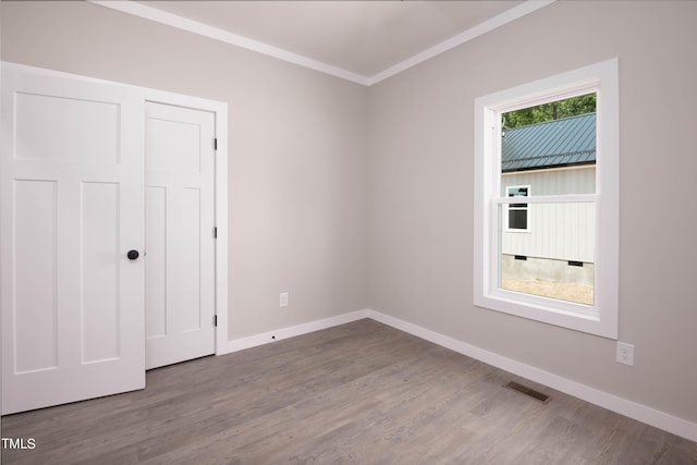 unfurnished bedroom with ornamental molding, multiple windows, wood-type flooring, and a closet