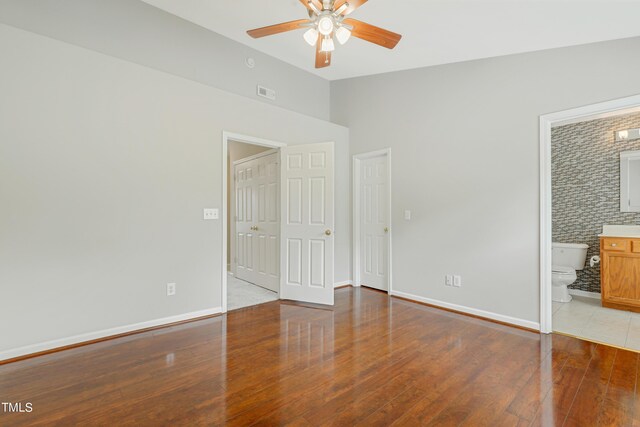 unfurnished bedroom with a closet, ensuite bathroom, wood-type flooring, and ceiling fan