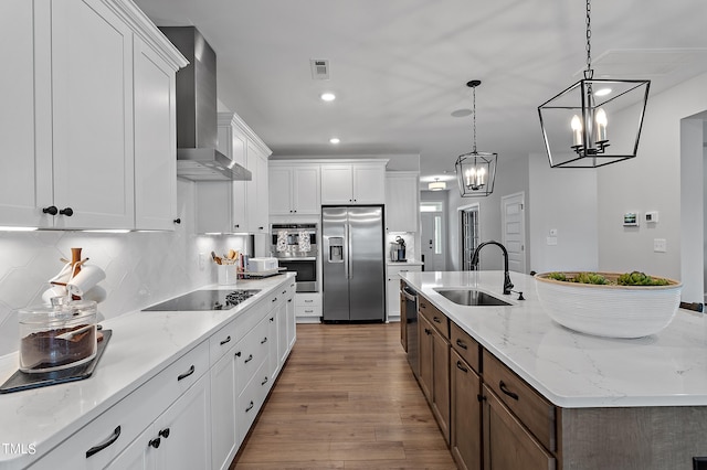 kitchen with sink, wall chimney exhaust hood, an island with sink, white cabinetry, and stainless steel appliances