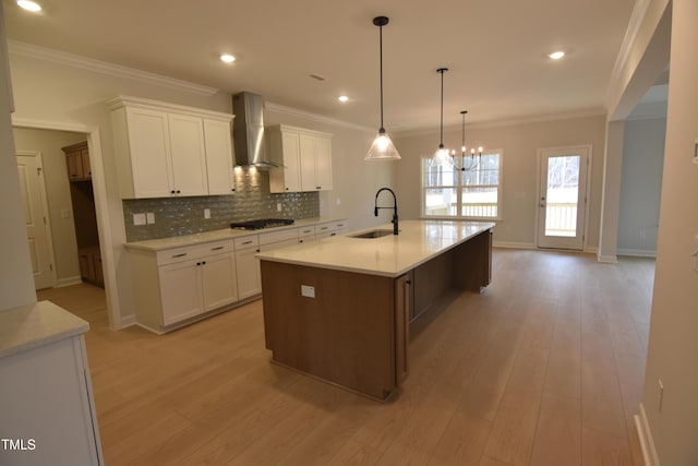 kitchen with white cabinetry, sink, wall chimney exhaust hood, an island with sink, and decorative light fixtures