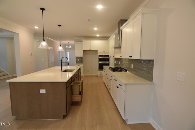 kitchen with a center island with sink, white cabinets, sink, and hanging light fixtures