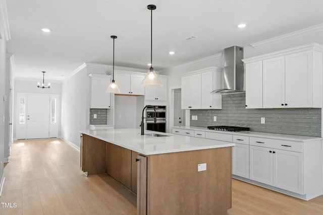kitchen with light countertops, white cabinets, a large island with sink, and wall chimney exhaust hood
