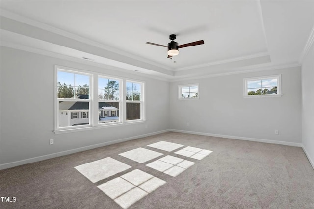 empty room with a tray ceiling, light colored carpet, crown molding, and baseboards