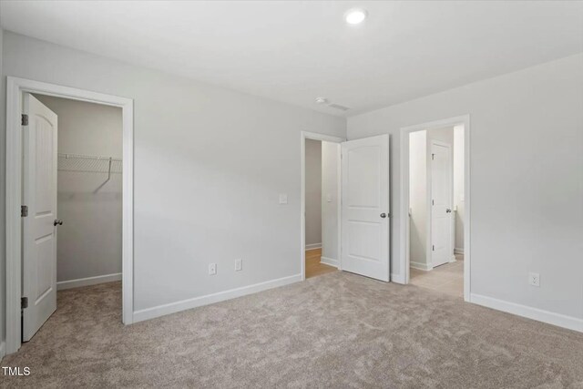 unfurnished bedroom featuring a walk in closet, a closet, light colored carpet, and baseboards