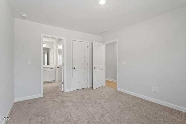 unfurnished bedroom featuring light carpet, ensuite bathroom, and baseboards
