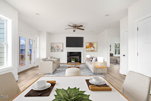 living room featuring ceiling fan, a tile fireplace, light hardwood / wood-style floors, and a healthy amount of sunlight